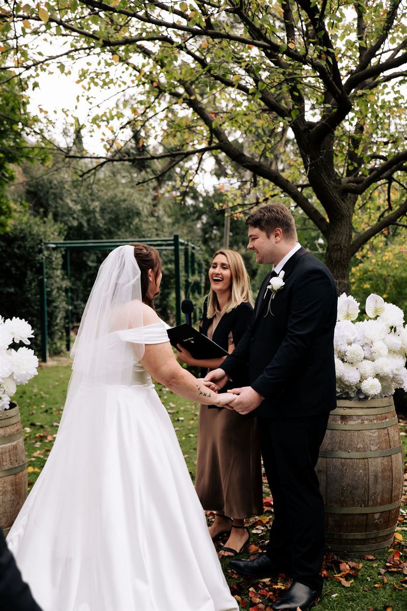 Adelaide celebrant Renée Melizza laughing with a bride and groom during their garden wedding ceremony, photo by Kirsty Caruso Photography