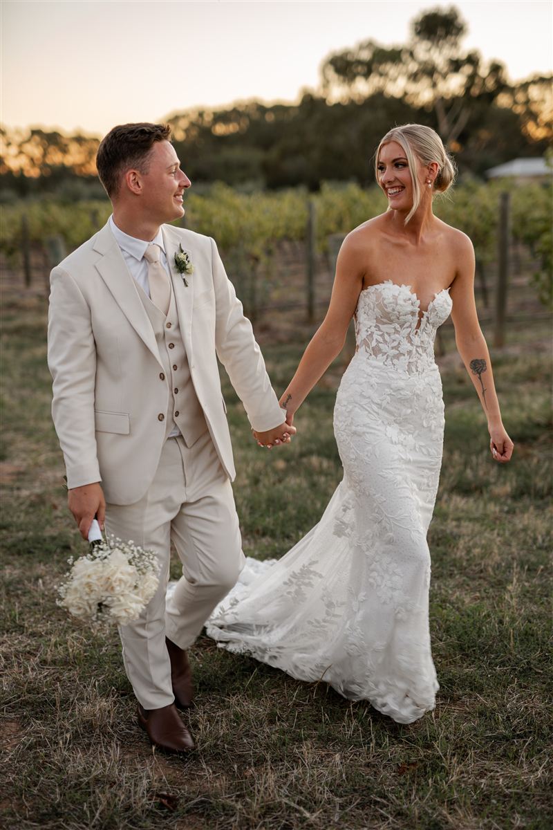 Catriona and Harry walking hand in hand through a vineyard at dusk after their wedding ceremony